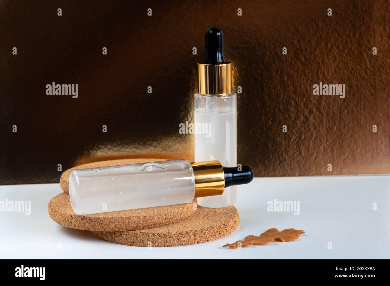 Auf einem weißen Tisch stehen zwei Milchflaschen mit einer Augenzange, isoliert auf einem goldenen Hintergrund auf Kork. Das Layout ist für das Design von Kosmetika geeignet. Stockfoto