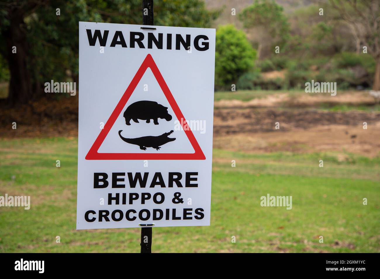 Nahaufnahme eines Schildes mit der Aufschrift „Vorsicht vor Nilpferden und Krokodilen“. Es gibt auch einen visuellen Hinweis auf ein Nilpferd und ein Krokodil in einem roten Dreieck. Stockfoto