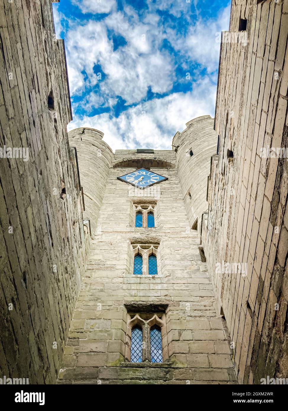 Blick auf das mittelalterliche Warwick Castle von unten mit dem wolkenblauen Himmel. Blick auf rustikale Steinmauern, dünne Fenster, eine Uhr und Turmtürme Stockfoto