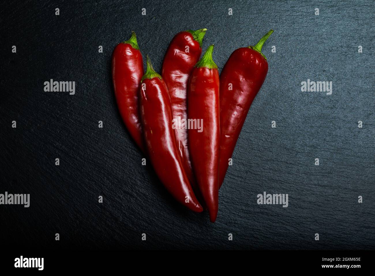Fünf Chilischoten auf schwarzem Schieferbrett. Flach liegend. Stockfoto