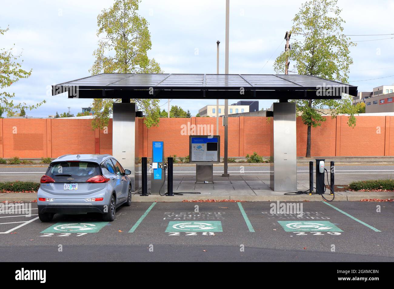 Eine Ladestation für Elektrofahrzeuge mit Sonnenschutzdach und ebike-Schließfächern für Batterieladegeräte auf dem OMSI-Parkplatz in Portland, Oregon Stockfoto