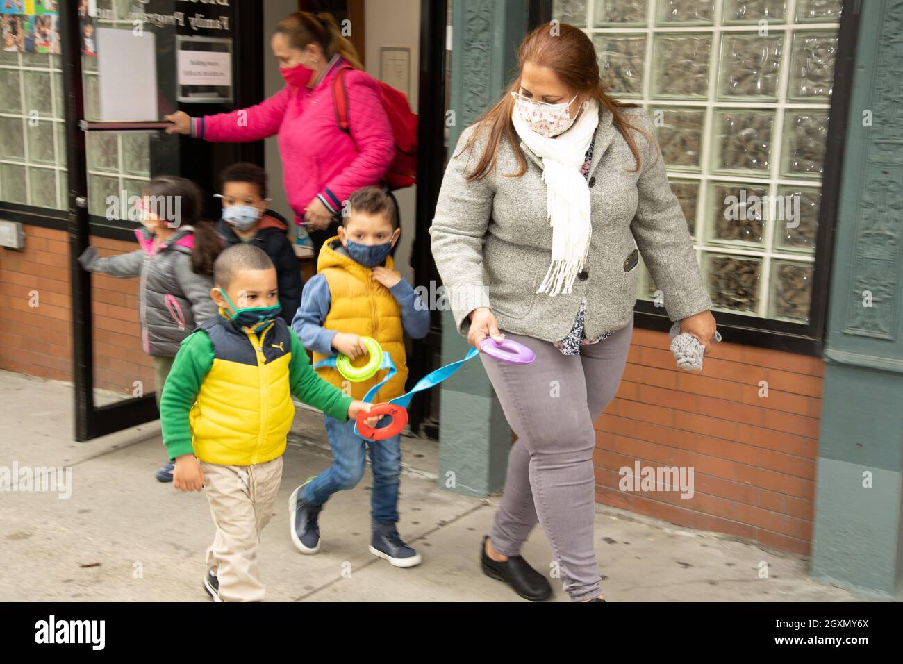 Bildung Vorschulgruppe von 3-Jährigen, die mit weiblichen Lehrern spazieren gehen, Gesichtsmasken tragen, Ringe am Seil festhalten, um zusammen zu bleiben Stockfoto