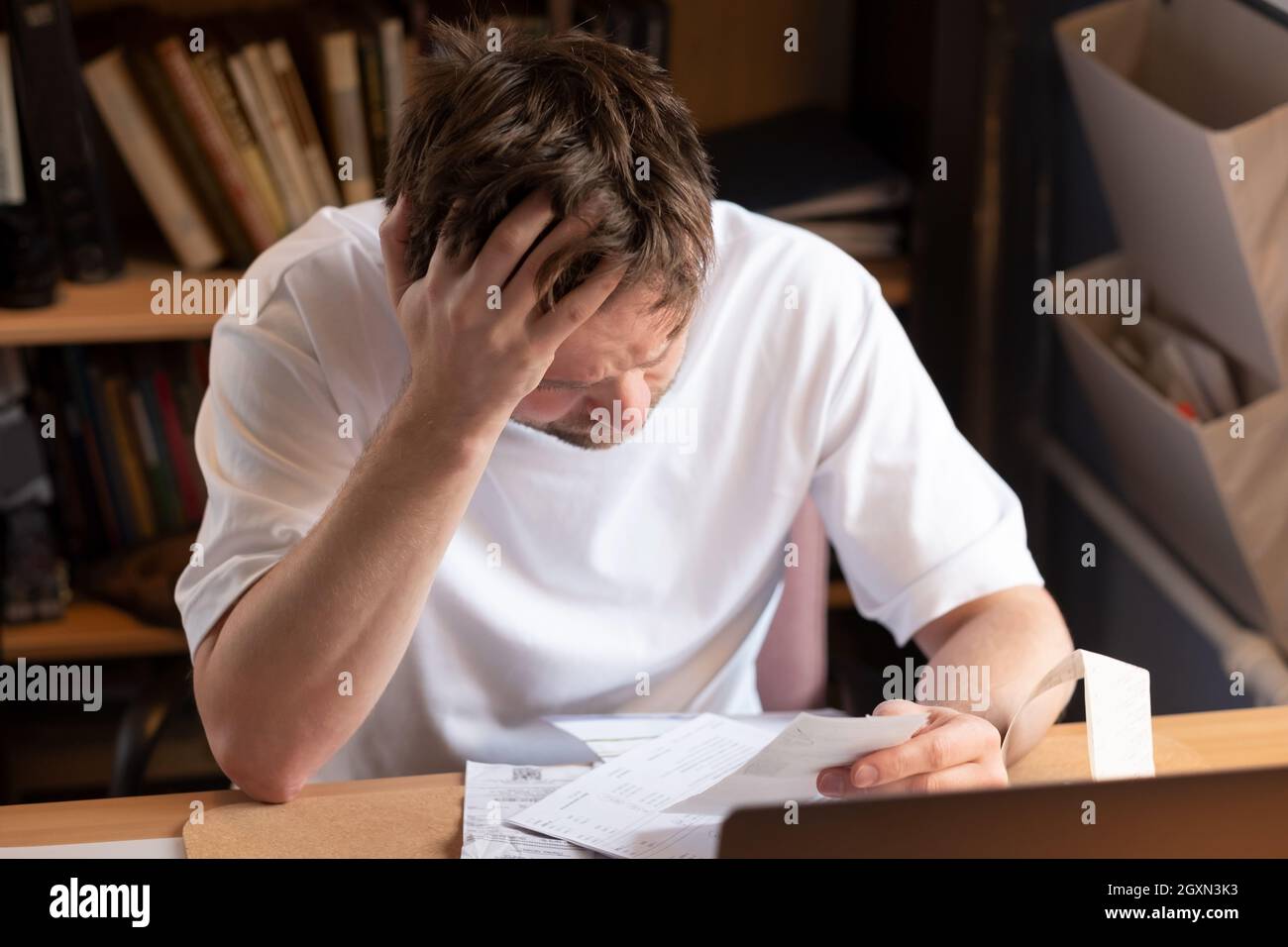 Mann, der zu Hause am Tisch sitzt, mit Papieren, die versuchen, sein Geld und seine Schulden zu zählen. Stockfoto