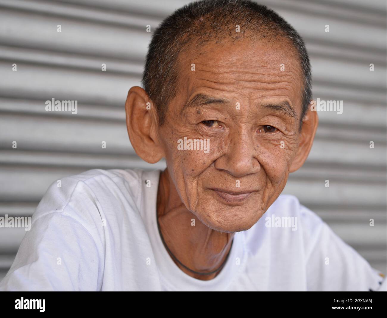 Der alte, dünne, einfallsreiche, positive malaysische, chinesische Trishaw-Rikscha-Fahrer mit eingewonntem Gesicht und faltiger Stirn blickt auf den Betrachter. Stockfoto
