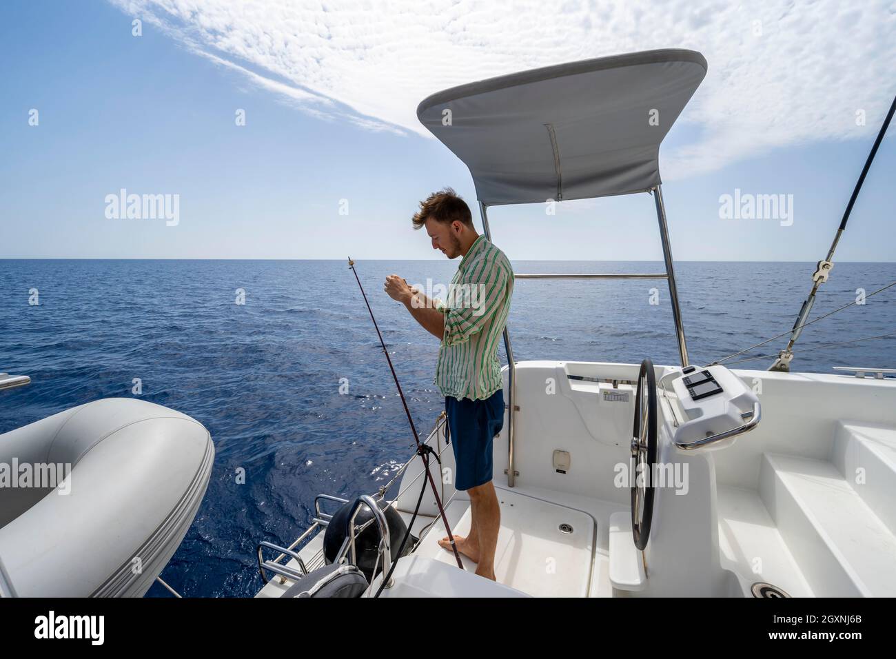 Junger Mann, der auf einem Boot fischt, Segel-Katamaran, Segeltörn, Dodekanes, Griechenland Stockfoto
