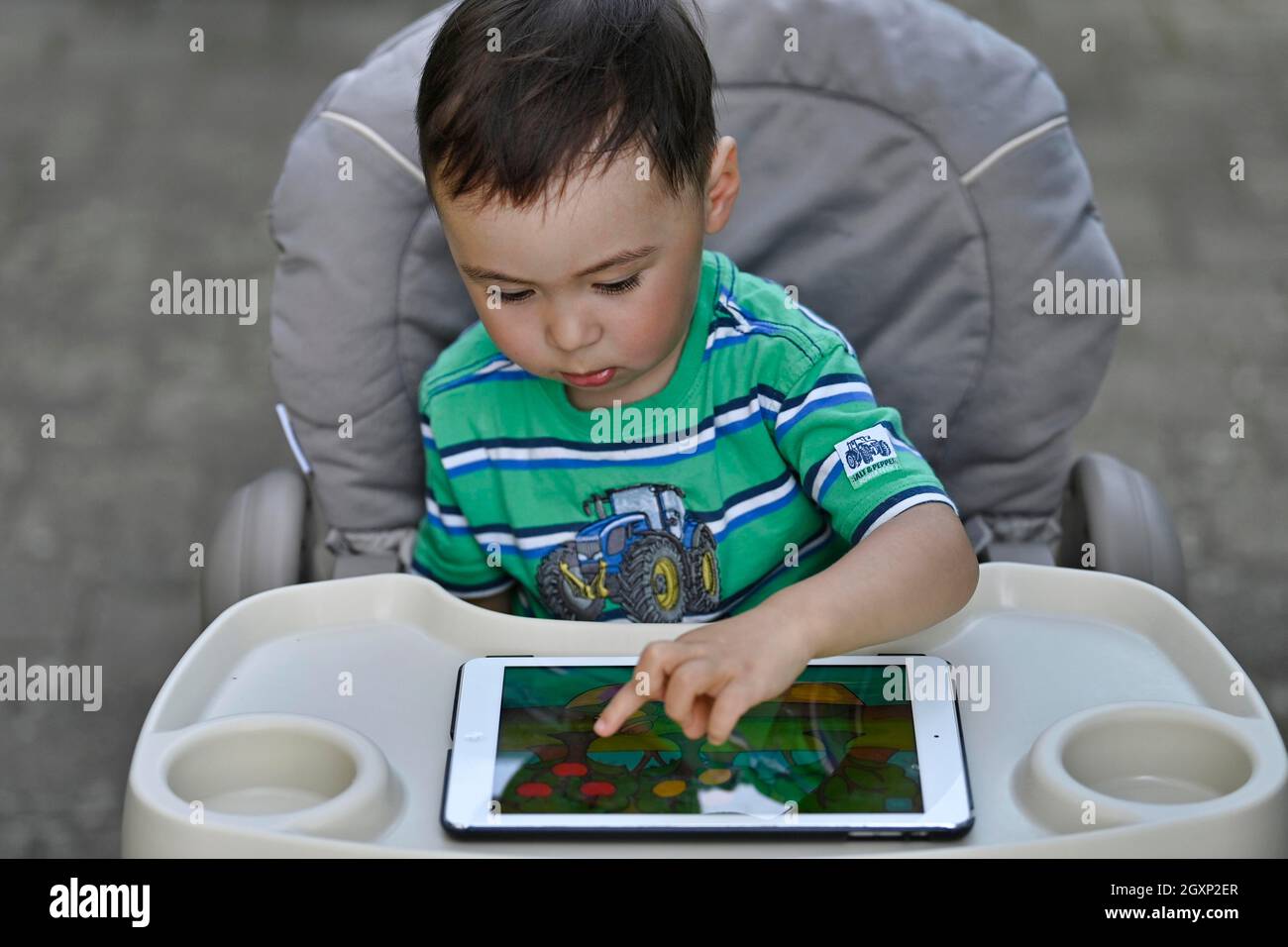 Kleinkind, 2 Jahre, multiethnisch, eurasisch, sitzt im Hochstuhl und spielt Lernspiel auf Tablet, Stuttgart, Baden-Württemberg, Deutschland Stockfoto