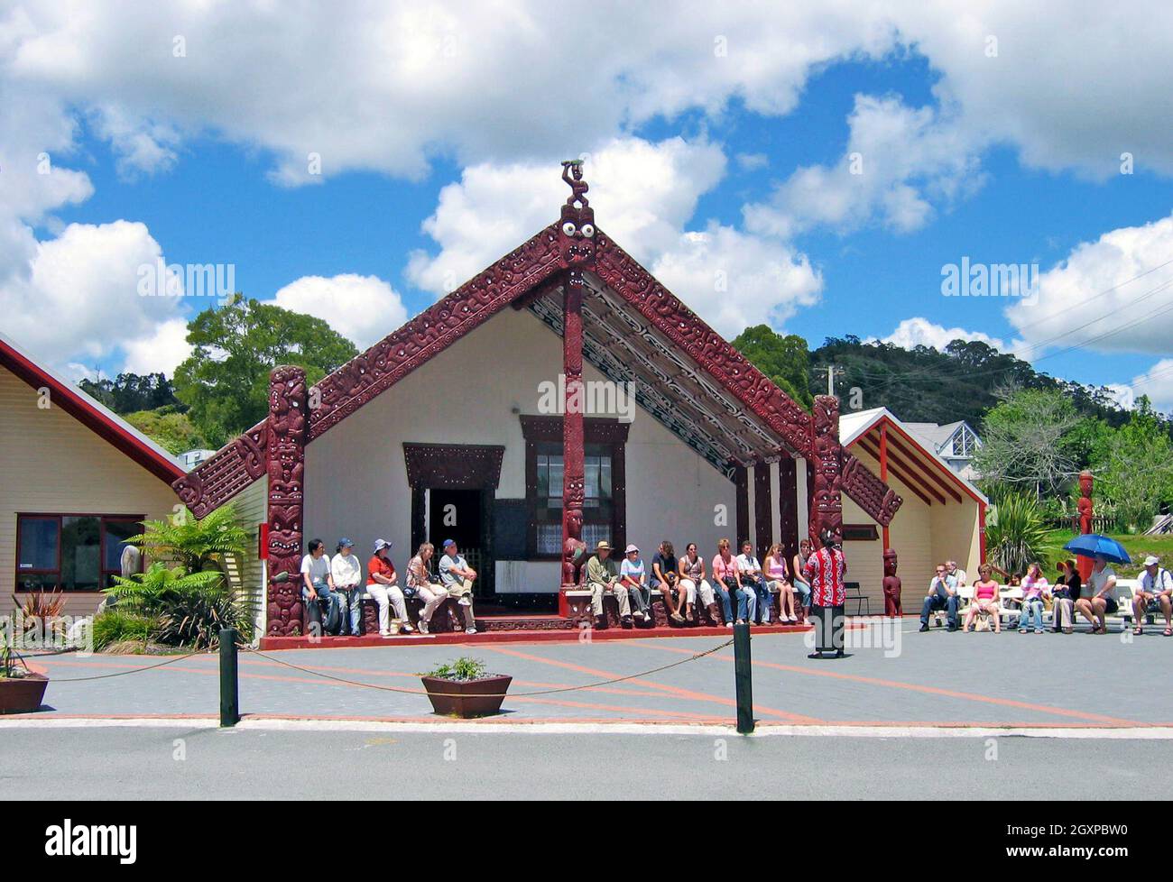 Touristen in Rotorua, Neuseeland, hören einem Führer zu, der über die Marae und das Maori-Dorf spricht, in dem sie sitzen. Indigener Tourismus und geothermischer Tourismus sind der Hauptanziehungspunkt für die Besucher dieses Lebensunterhaltungsgeldes, in dem Familien leben, arbeiten und die Umwelt respektieren, in der sie leben. Stockfoto
