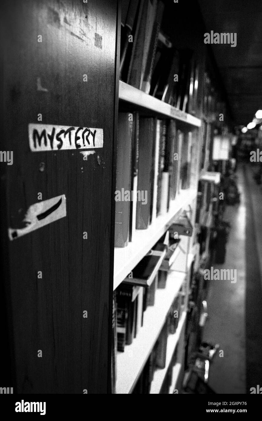 Schwarz-Weiß-Tiefenaufnahme einer Reihe von Büchern in der Mystery-Sektion einer Bibliothek oder Buchhandlung Stockfoto