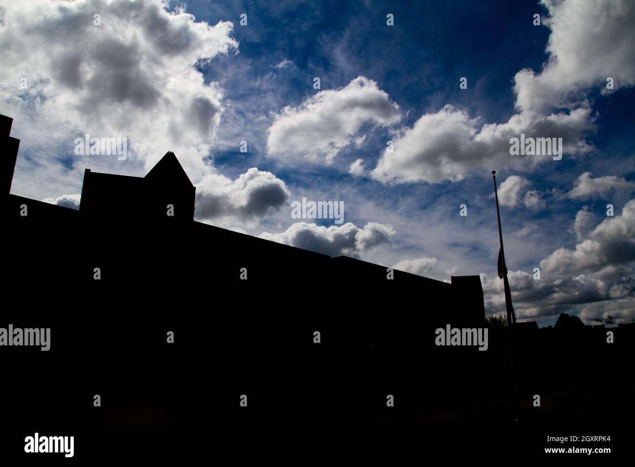 Große Gebäude und ein Fahnenmast mit Hintergrundbeleuchtung und Silhouetten gegen einen teilweise bewölkten Himmel Stockfoto