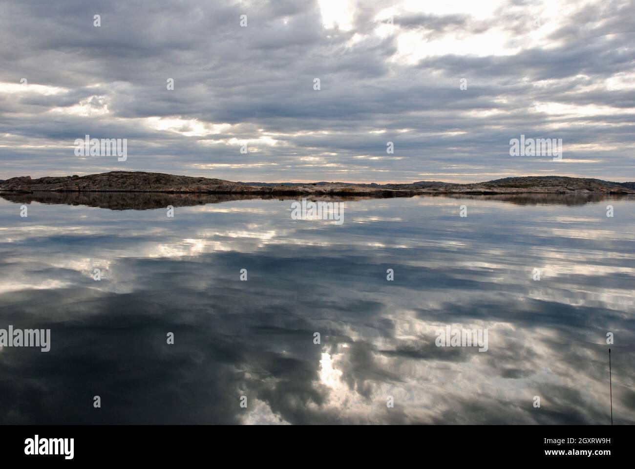 Spiegelungen von Wolken auf ruhigen Morgenmeeren nur wenige Minuten vor Sonnenaufgang im Fjällbacka-Archipel an der Westküste Schwedens Stockfoto
