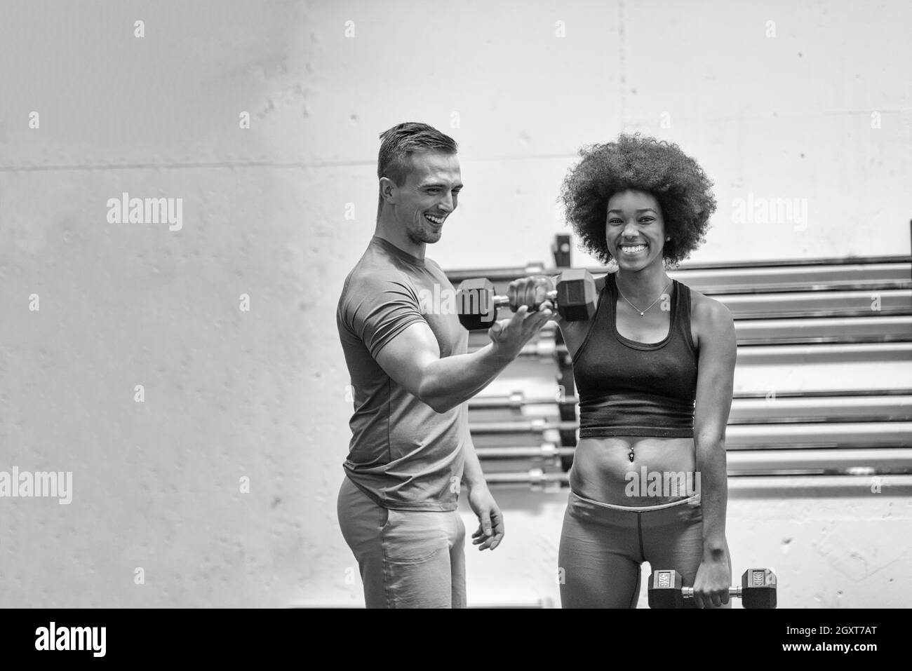 junge schöne afroamerikanische Frau tun Bizeps-curls mit Fitness-Trainer in einem Fitnessstudio Stockfoto