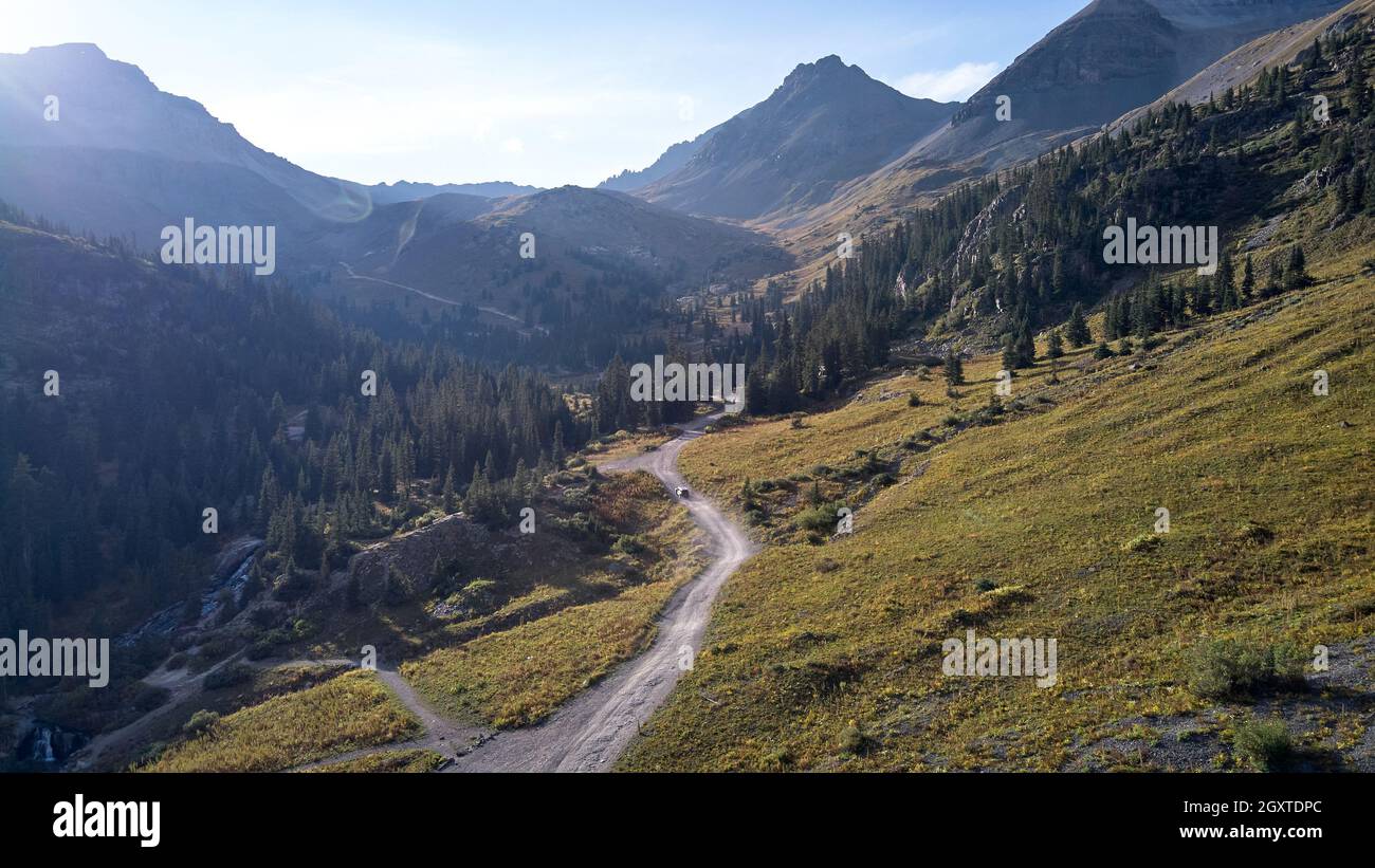 Unbefestigte Straße mit Jeep, der durch ein riesiges Tal in den Colorado Bergen fährt Stockfoto