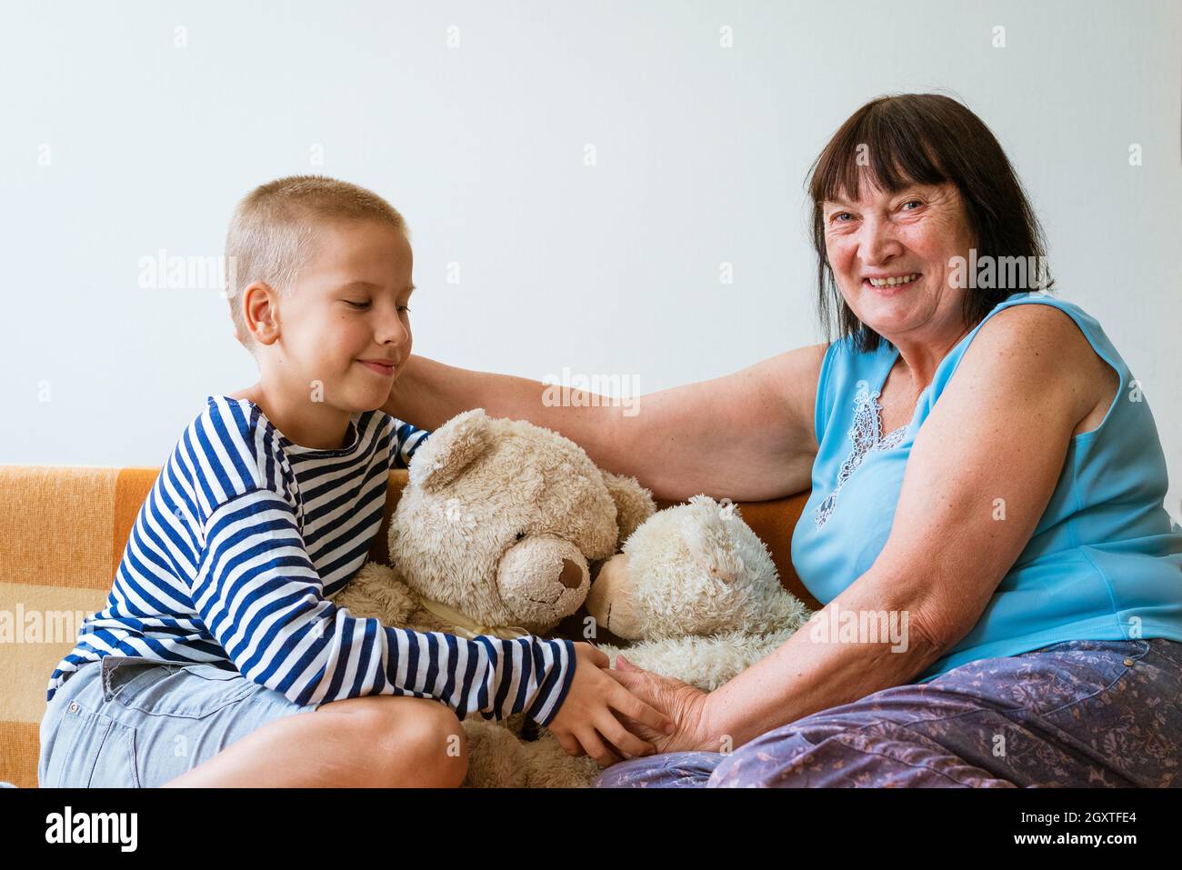 Kind spielt mit einer alten Großmutter und einem Teddybären-Spielzeug. Fröhliche und lächelnde Großmutter mit ihrem Enkel. Niedliches Kleinkind Junge spielt mit älteren Frau sitzen auf dem Sofa zu Hause Stockfoto