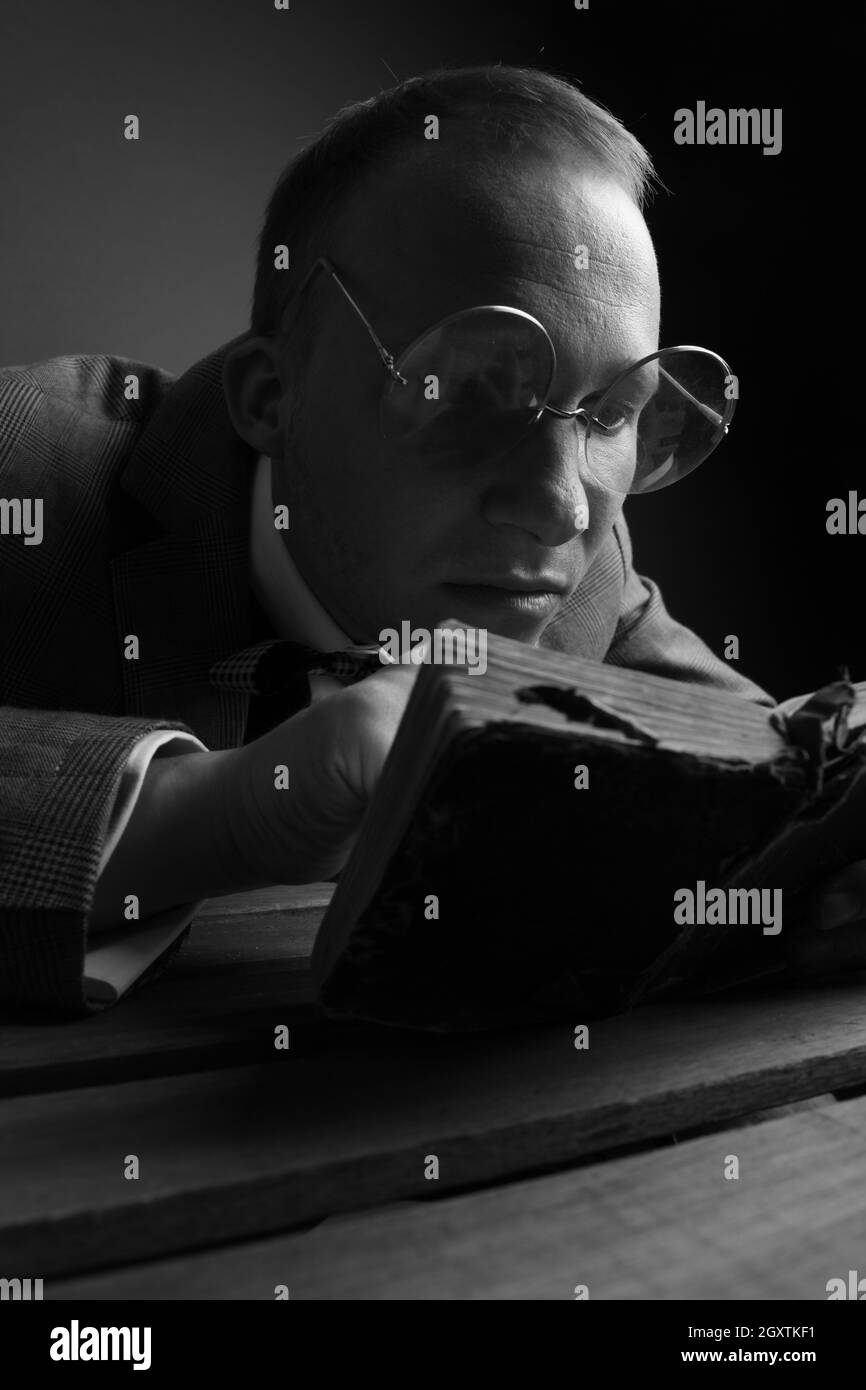Schwarzweiß-Foto. Porträt eines Mannes.Ein komischer, humorvoller, fröhlicher Kerl in braunem Anzug und Brille, der ein Buch in den Händen hält, untersucht das Buch genau. Hochwertige Fotos Stockfoto