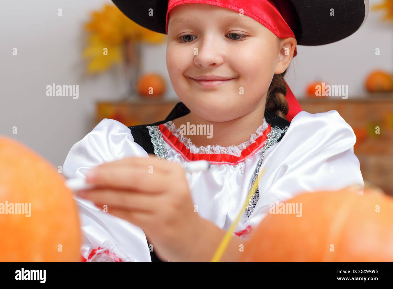 Halloween zu Hause feiern. Nahaufnahme eines kleinen Mädchens, das als Pirat gekleidet ist. Das Kind bereitet sich auf die Party vor und zieht den Kürbis an. Stockfoto