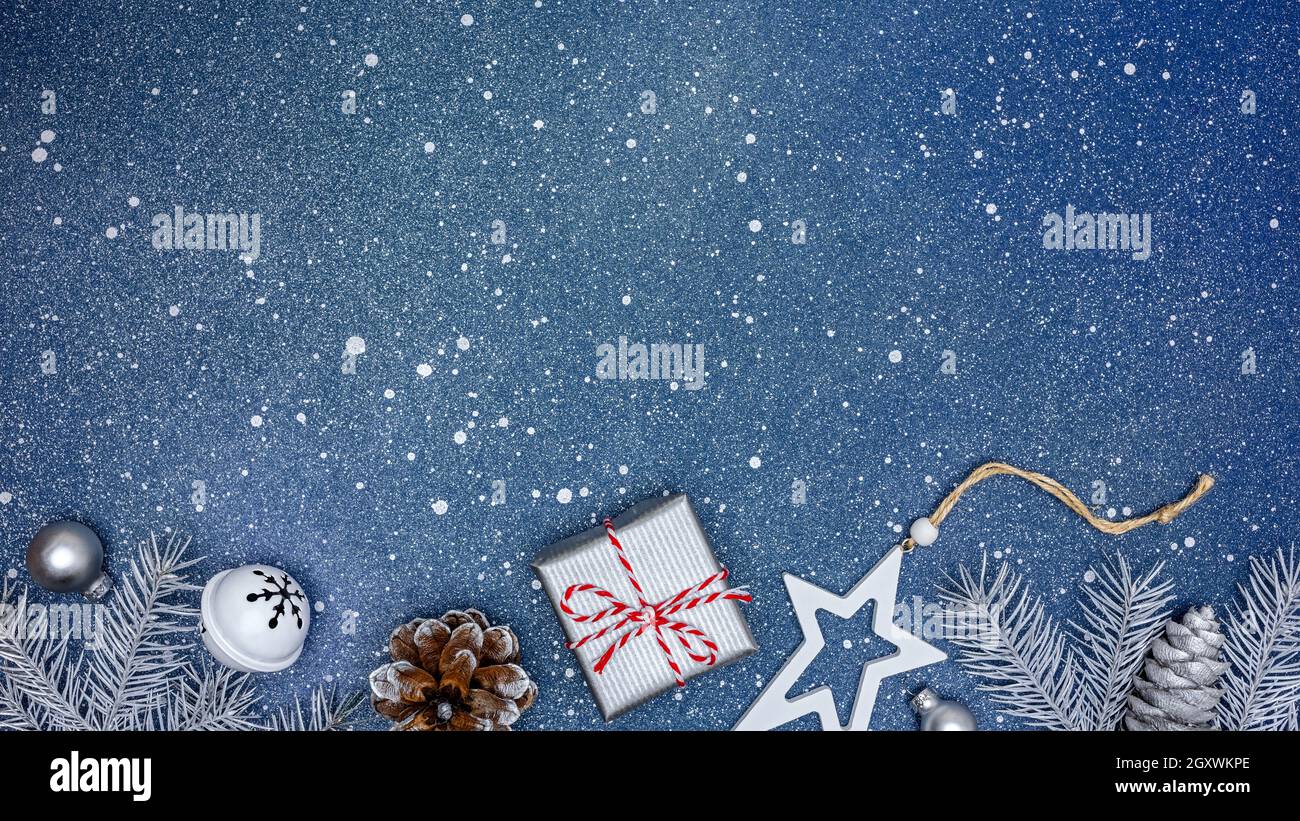 weihnachts-Geschenkbox mit Jingle-Glocke, Tannenzapfen, Holzstern und Tannenzweigen auf blauem Hintergrund. Flach liegend. Stockfoto