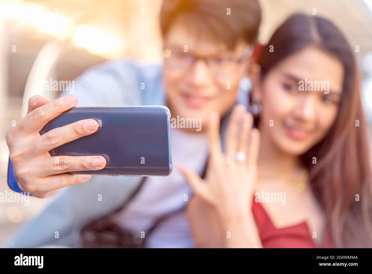 Blurry of Happy Young Woman showing Diamond rings on Finger to boyfriend Selfie on phone. Neu verlobt Mädchen und Verlobten im Hintergrund. Verlobter Lo Stockfoto