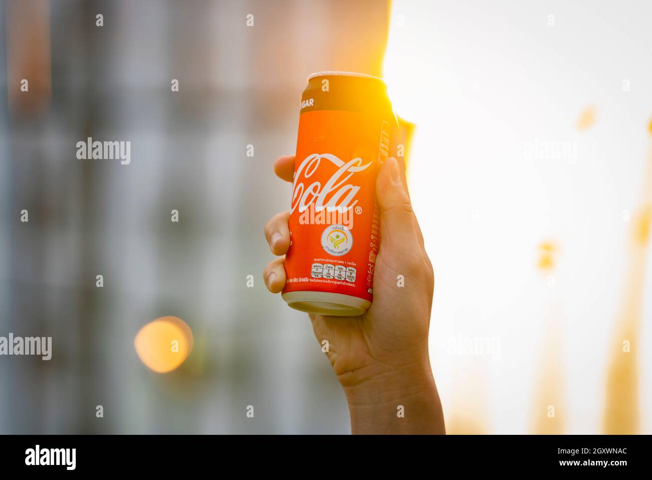 Coca Cola Getränk in der Hand. Kerl, der Dose zum Sonnenlicht aufsteigt. Mann hält und trinkt Cola Dose mit glücklichen Gesicht bei Sonnenuntergang. BANGKOK, THAILAND - FEBRUAR 2 2020. Stockfoto