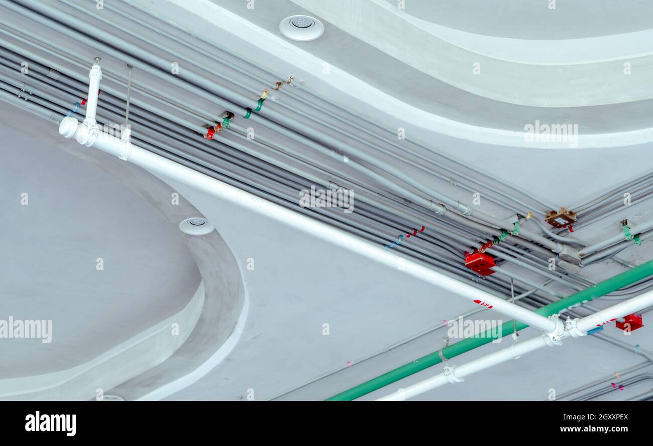 Elektrisches Rohrsystem und verzinktes Stahlrohr mit Elektrokabel an der Decke installiert. Automatische Brandschutzanlage mit weißem Rohr Bu Stockfoto