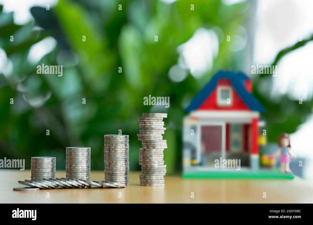 Ein Haufen Münzen brechen zusammen. Mini Holzhaus und Reihe von Münzen fällt. Hypothek- und Immobilieninvestition oder Versicherungsfinanzierung und Anlagekonzept. Stockfoto