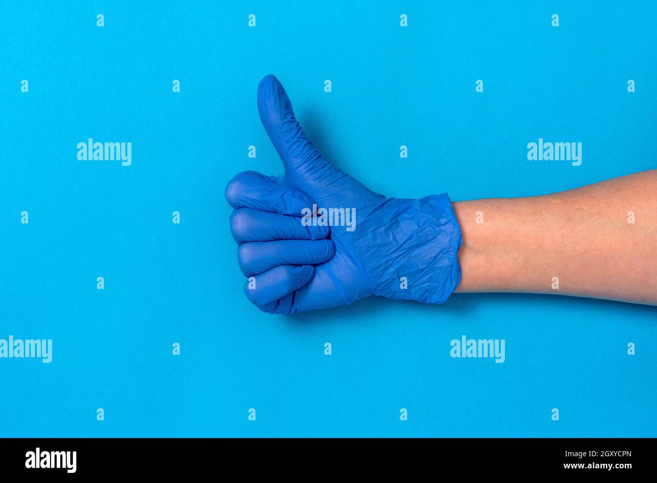 Hand in einem blauen Gummihandschuh mit Daumen nach oben Blauer Hintergrund Stockfoto