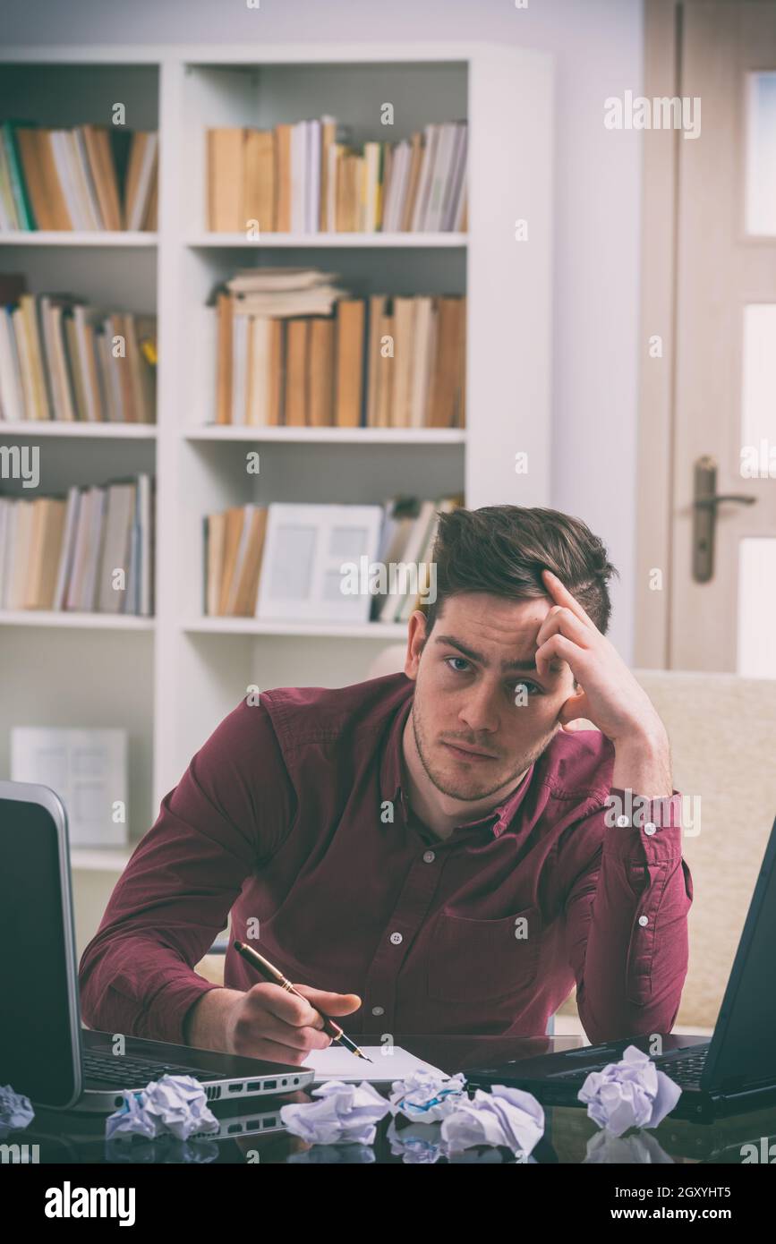 Ein Schriftsteller, Blogger oder Mitarbeiter, der unter einem Mangel an kreativer Energie leidet, Inspiration mit Stift in der Hand sitzend in seinem Zimmerbüro. Stockfoto