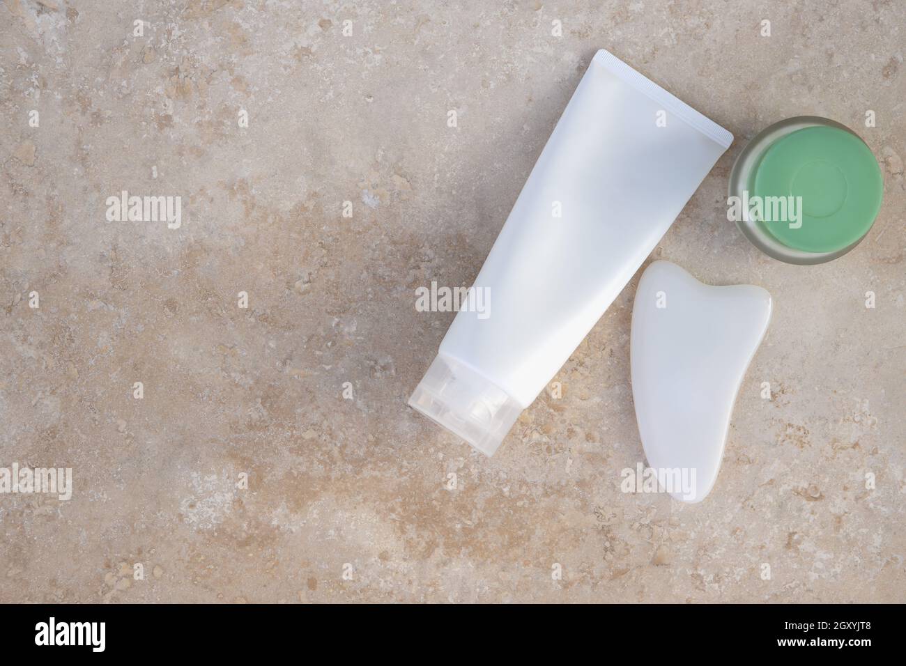 Beauty-Set. Weißes Gua Sha Scraper-Massagegerät, schäumendes Gel, Creme auf leicht strukturierter Oberfläche. Platz zum Kopieren, flach liegend. Konzept Schönheit, Selbstpflege, Gesicht Körper c Stockfoto