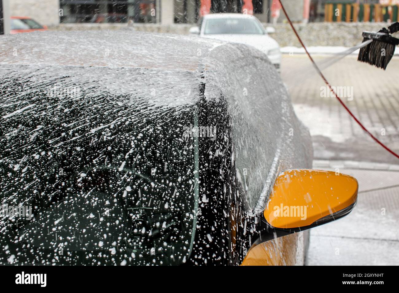 Gelbe Auto fast vollständig in Shampoo Schaum bedeckt, mit mehr spritzen, wenn in der Waschstraße gewaschen. Stockfoto