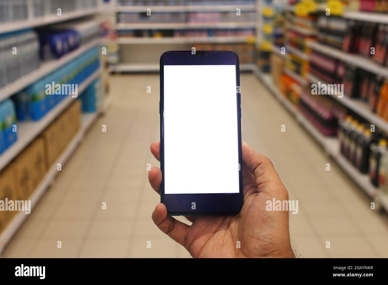 Smartphone mit leerem weißen Bildschirm. Hand hält Smartphone mit verschwommenem Supermarkt Gänge Hintergrund. Online-Shopping-Konzept. Stockfoto