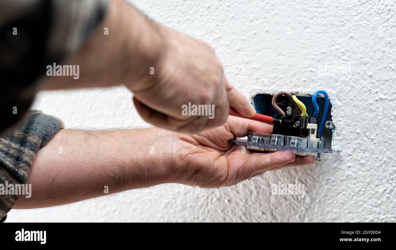 Elektriker mit Schraubendreher fixiert elektrische Kabel in den Anschlüssen der Steckdose eines elektrischen Systems. Bauindustrie. Stockfoto