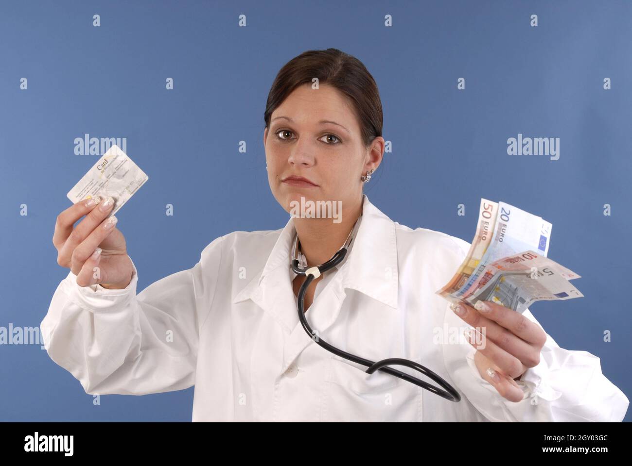 Zuckende Schultern junge Ärztin mit Stethoskop zeigt Geld und Krankenversicherungskarte Stockfoto