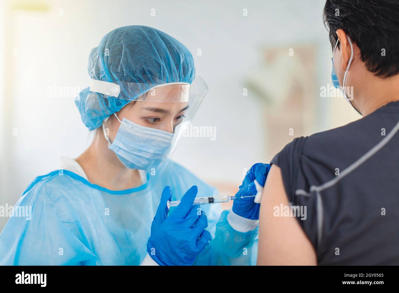 Der Arzt oder die Krankenschwester trägt Kleider, Masken und Augenmasken, um einem Patienten bei der Injektion zu helfen Stockfoto