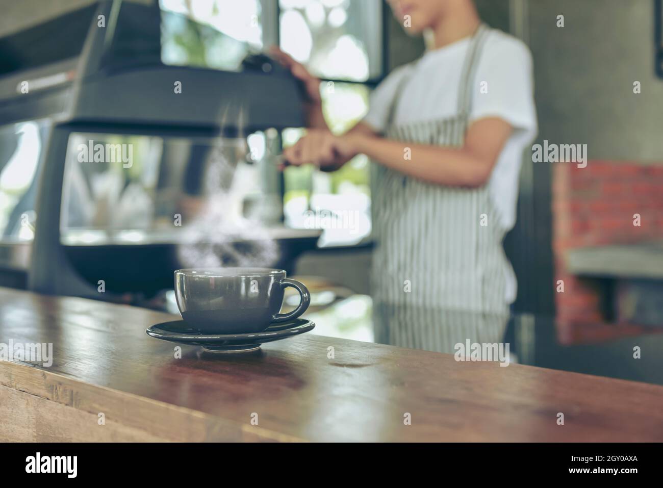 Der junge Besitzer des Cafés steht an der Theke. Der junge asiatische Barista lächelt und verwendet eine Kaffeemaschine an der Theke des Cafés, um Getränke zuzubereiten. Essen Stockfoto
