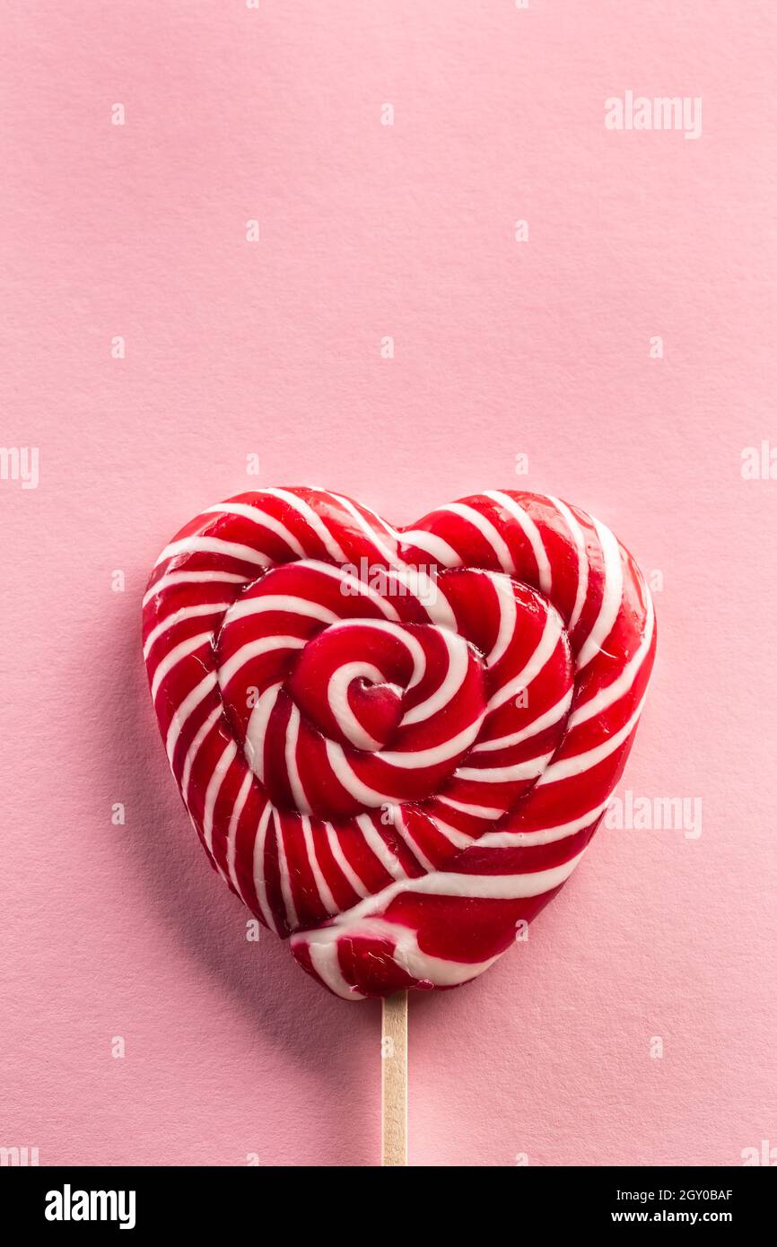 Köstlich aussehender süßer herzhafter Lollipop, der auf einem Holzstab mit Rose im Hintergrund genäht ist. Stockfoto