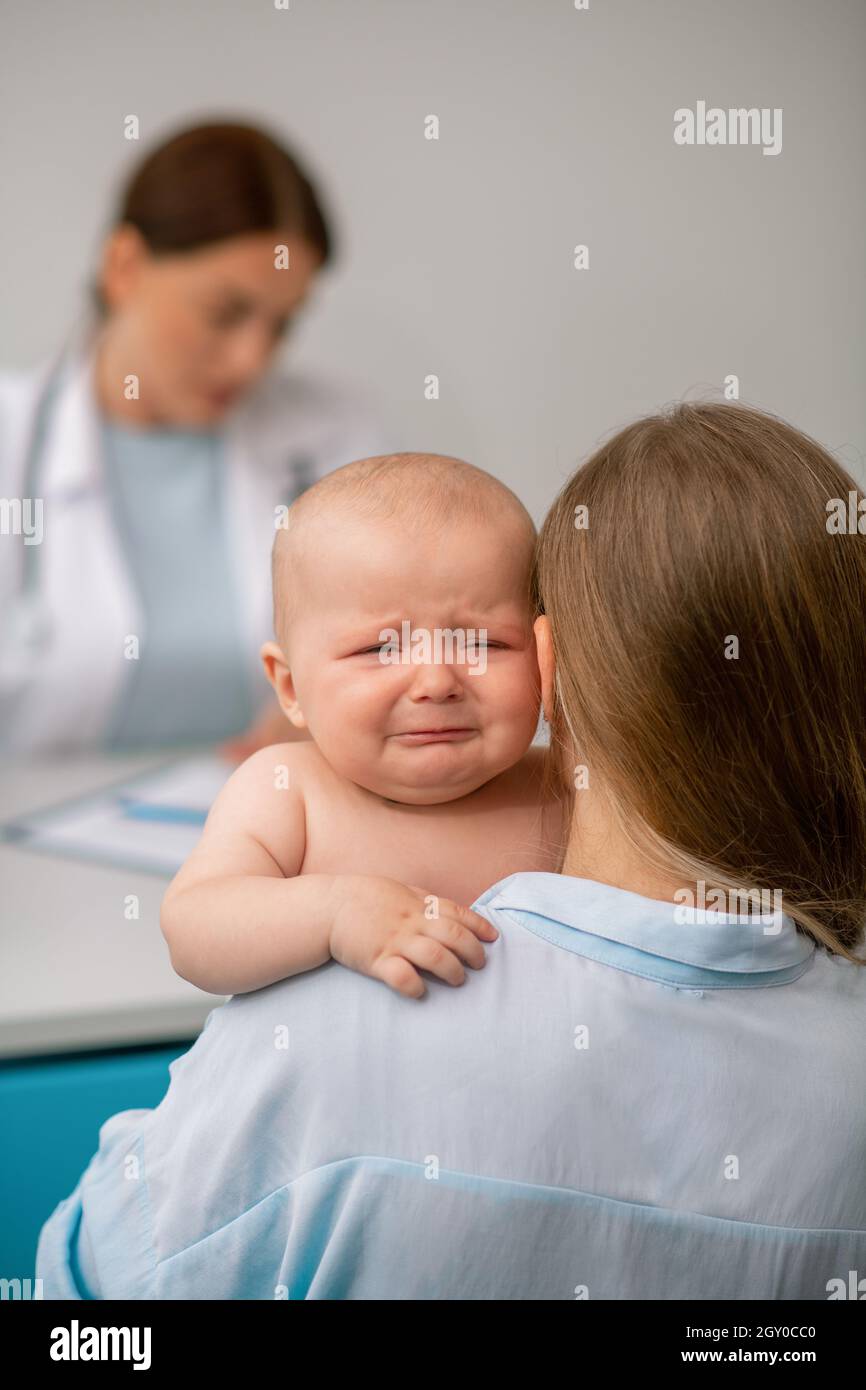 Weibliche Eltern halten ihr verärgertes Baby im Kinderarztbüro Stockfoto