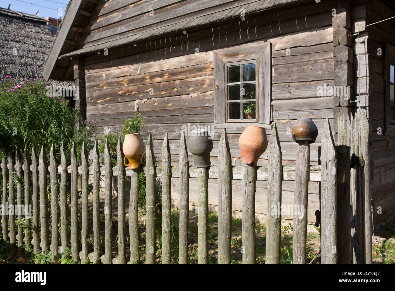 Töpfe für einen rustikalen Holzofen, trocknen auf einer rustikalen Holzpalisade. Vor dem Hintergrund eines alten Holzhauses. Stockfoto