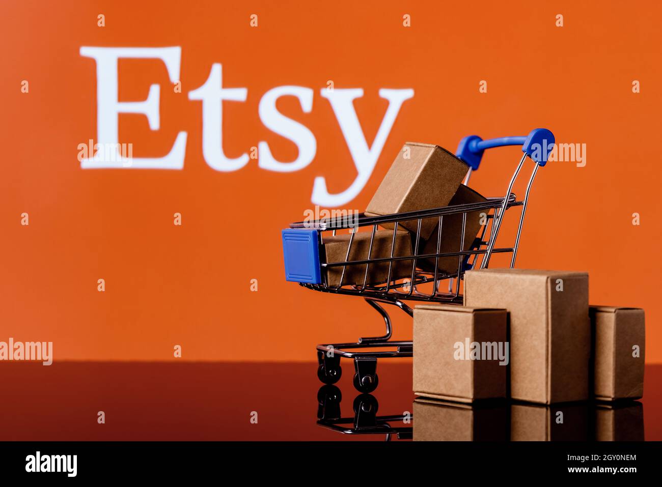 Warenkorb mit Paketen auf dem Hintergrund des Etsy-Logos. Stockfoto