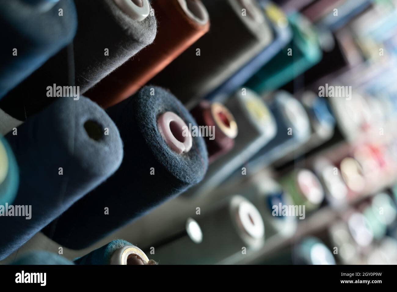 In einer Nähwerkstatt hängen viele Garnspulen verschiedener Farben an einer Metallwand. Schneiderkonzept. Stockfoto