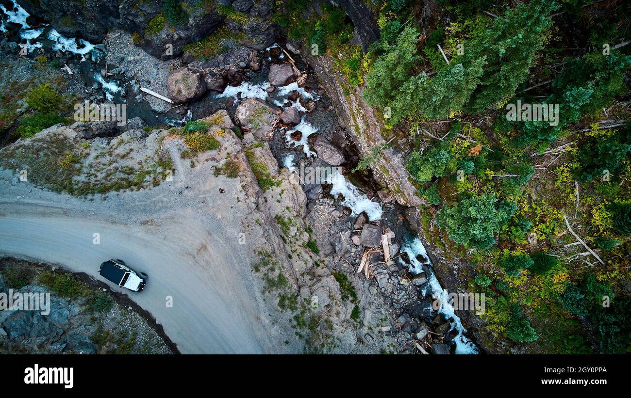 Luftaufnahme auf unbefestigte Straße mit weißem Jeep in der Nähe von Klippen mit Stromschnellen unten Stockfoto