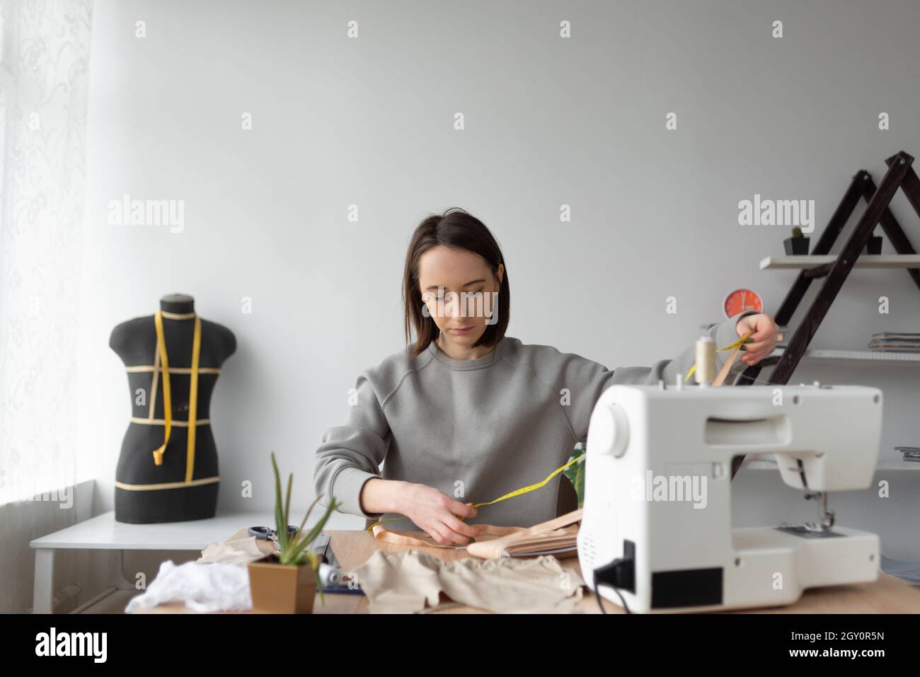 Eine Näherin im Hintergrund ihrer Werkstatt ist mit dem Nähen von Kleidung beschäftigt. Stockfoto