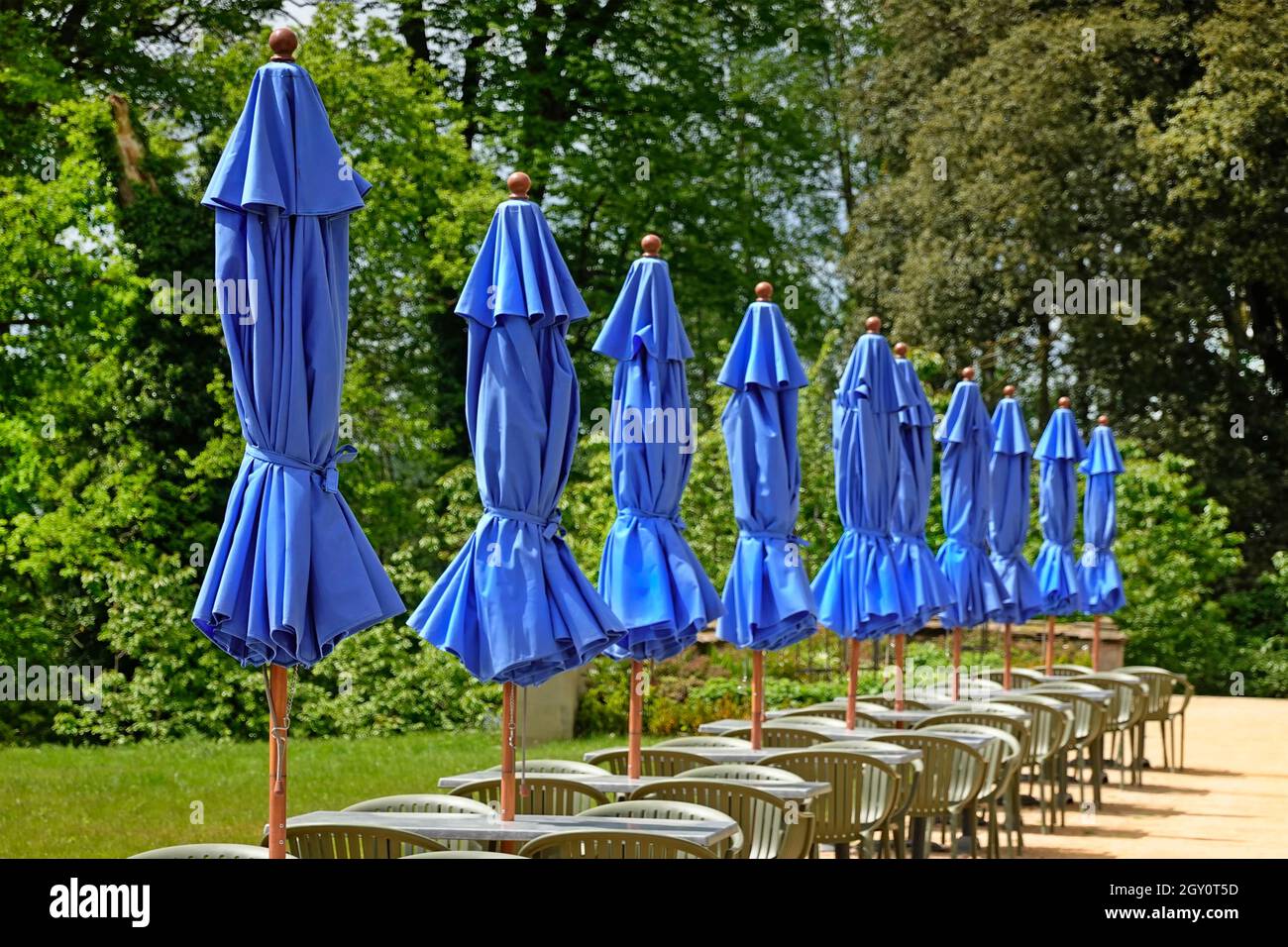 Eine Reihe von Tischen im Freien, Stühle und gefaltete blaue Sonnenschirme vor der Hotelbar, da das Wetter in der Sommersaison zu kalt und windig für Gäste im Mai-England ist Stockfoto