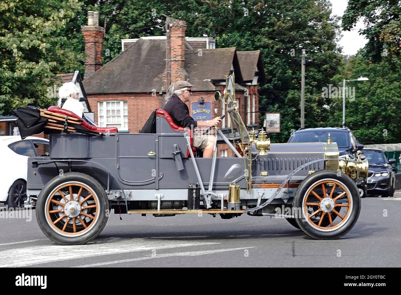 Seitenansicht älterer männlicher Fahrer und Passagiere auf einem historischen Cabriolet mit offenem Oberdeck, das die Straßenkreuzung im Stadtzentrum von Billericay überquert, Straßenszene in Großbritannien Stockfoto