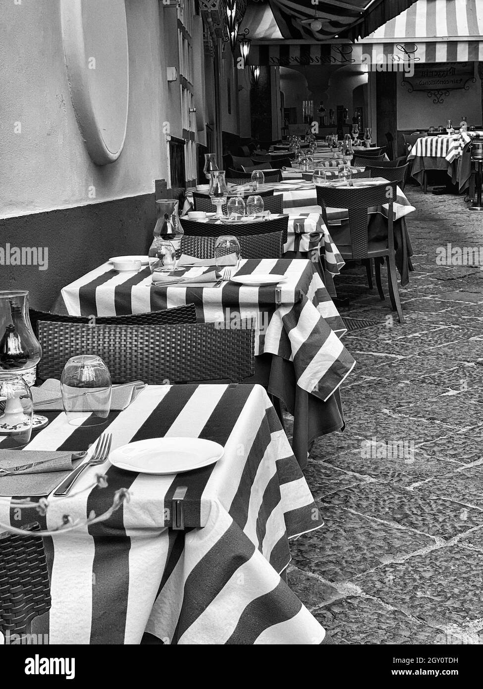 Graustufen-Aufnahme von gedeckten Tischreihen im Freien auf der Café-Terrasse Stockfoto