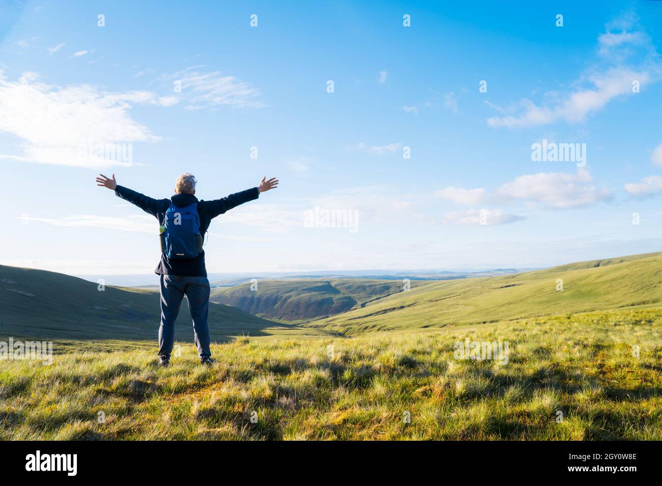 Rückansicht Mann Wanderer mit Rucksack stehen auf dem Berg mit erhobenen Händen und genießen Talblick. Reise Lifestyle Fernweh Abenteuer. Weg zu G Stockfoto