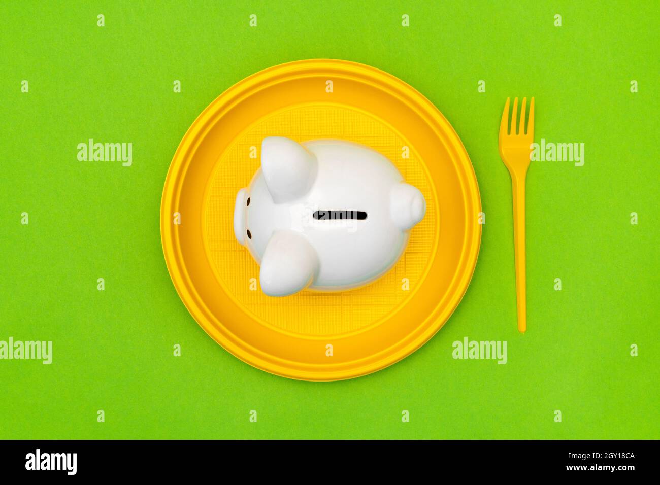 Sparkonzept für Verbraucher. Sparschwein auf dem gelben Einwegteller mit einer Gabel. Stockfoto