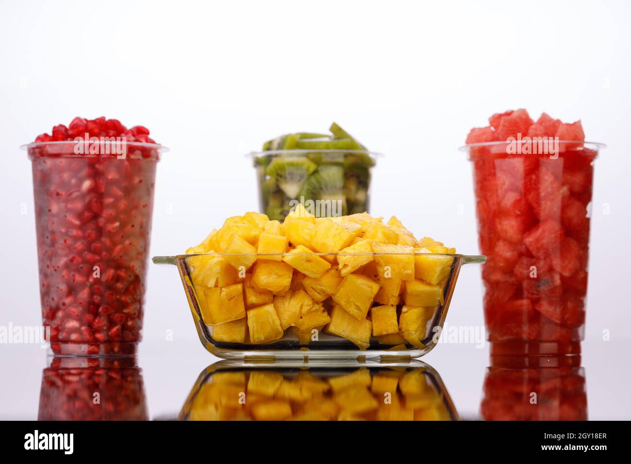 Wassermelone, Ananas, Granatapfel und Kiwi-Scheiben in transparenten Gläsern mit weißem Hintergrund, isoliert Stockfoto