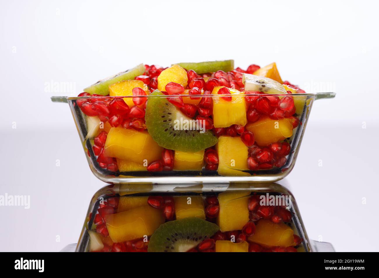 Gemischte geschnittene Früchte in einer durchsichtigen Glasschale mit weißem Hintergrund, isoliert. Stockfoto