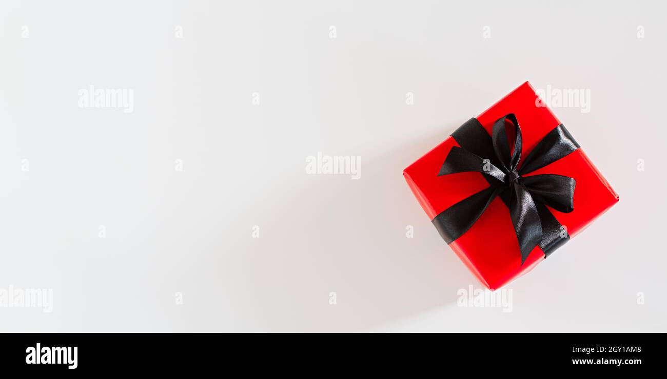 Geschenk schwarz und rot Verpackung. Draufsicht auf ein helles Geschenk mit einem schwarzen Satinband auf weißem Hintergrund. Konzeptuelles minimalistisches Bannerdesign für Bir Stockfoto