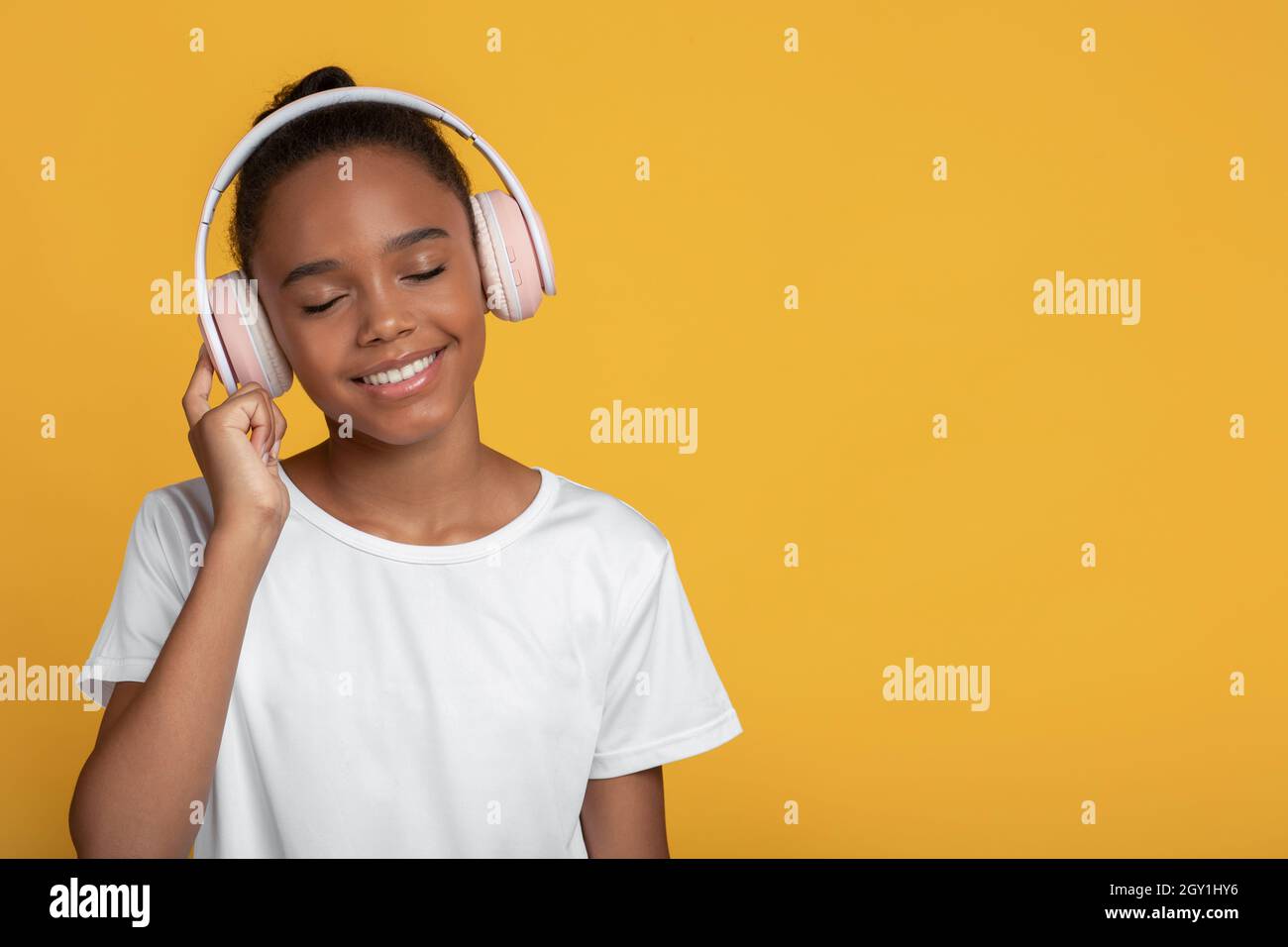 Lächelndes afroamerikanisches Mädchen im Teenageralter in weißem T-Shirt in Kopfhörern mit geschlossenen Augen hören Musik Stockfoto