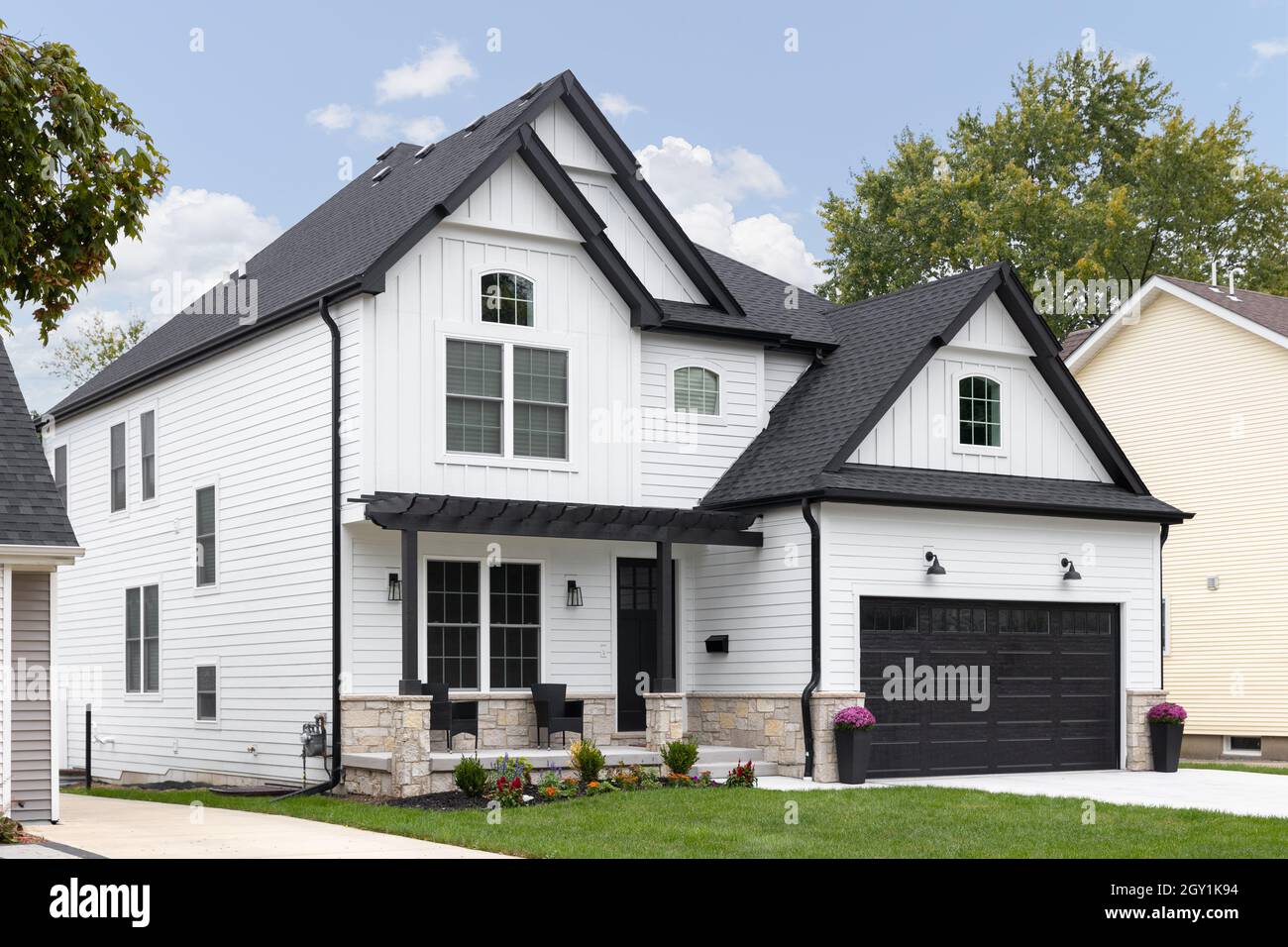 Ein traditionelles, modernes Bauernhaus mit weißem Dach, schwarzem Dach und Garagentor und einer überdachten Veranda. Stockfoto